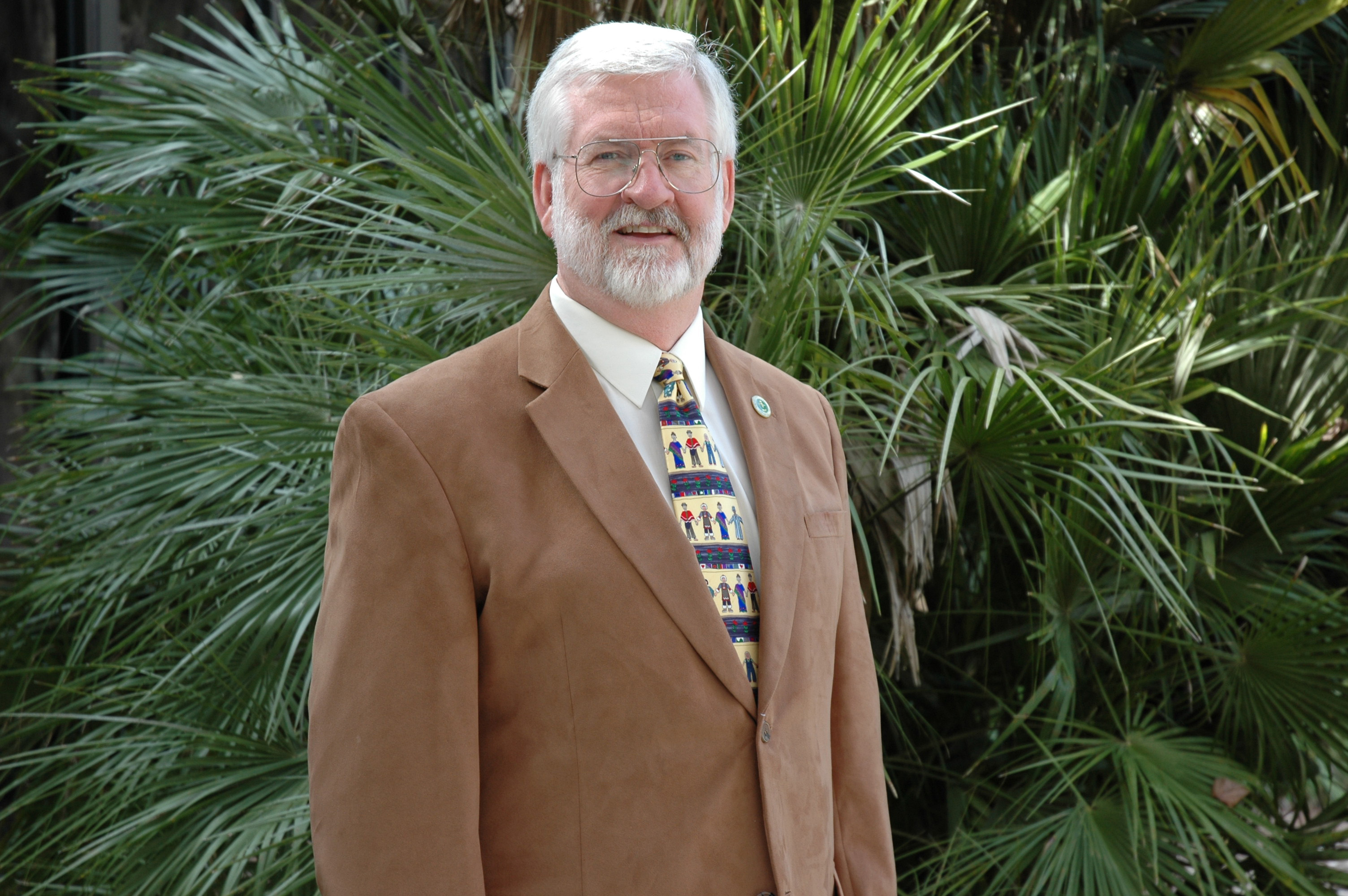 Man in a tan suit in front of palm tree