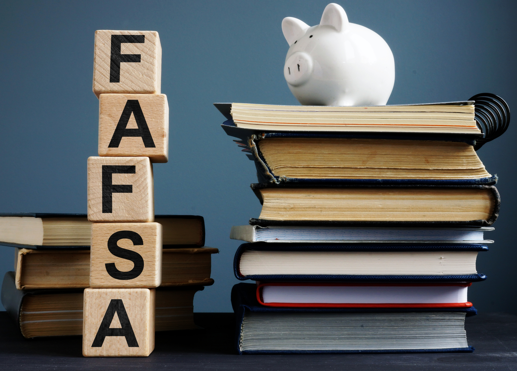 Stacked books with piggy bank on top and stacked FAFSA block Letters