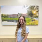 Woman in blue shirt standing in front of a large photo print of the FGC Library