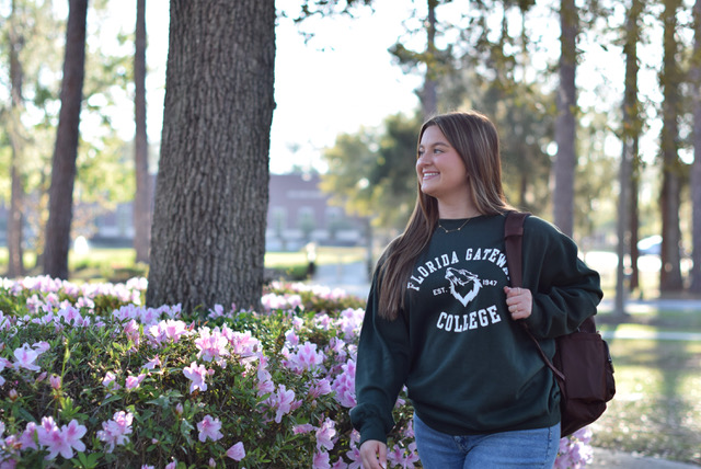 Female student in FGC Sweatshirt smiling in front of tree