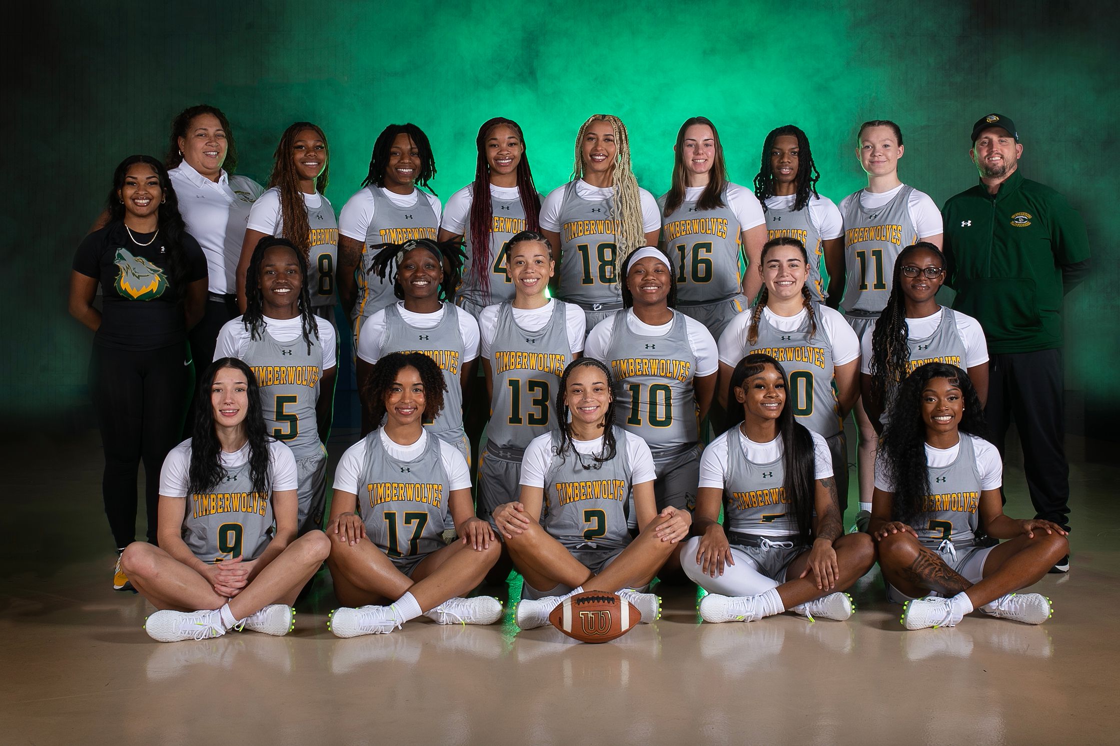 Posed photo of women's flag football team and coaches with green background.