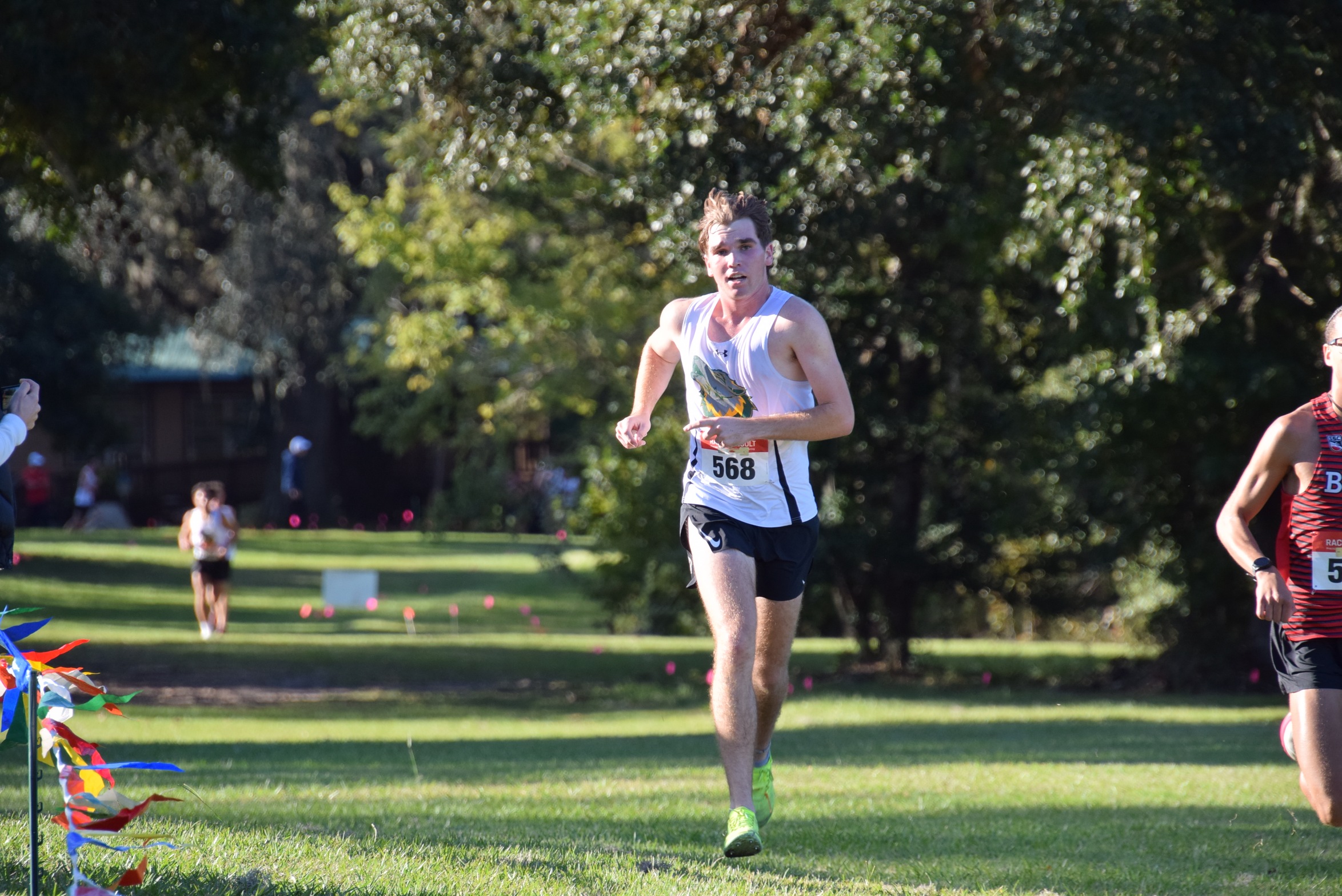 FGC Men's Cross Country runner running in race in grassy park.