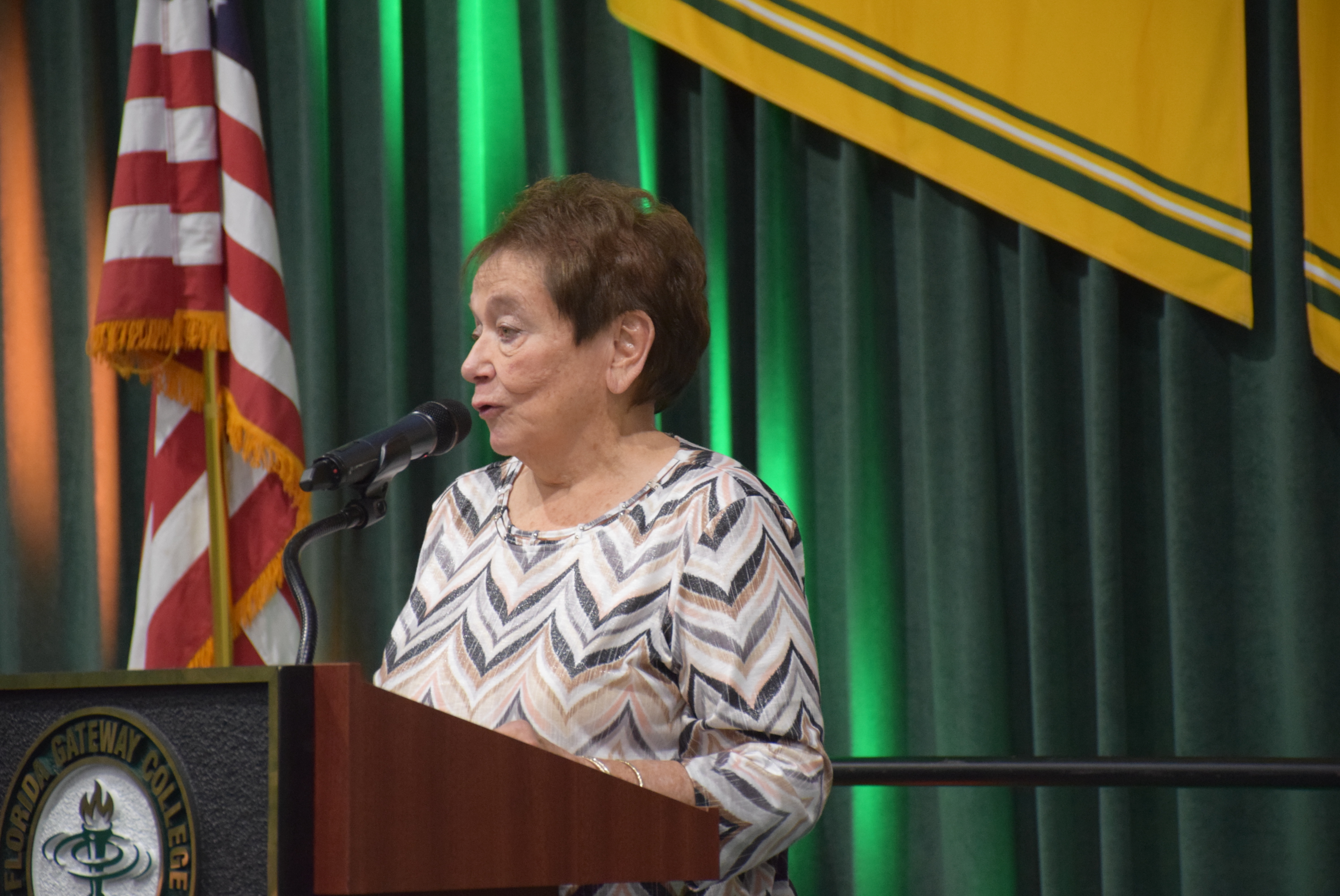 A woman speaks a podium; green curtain behind her.