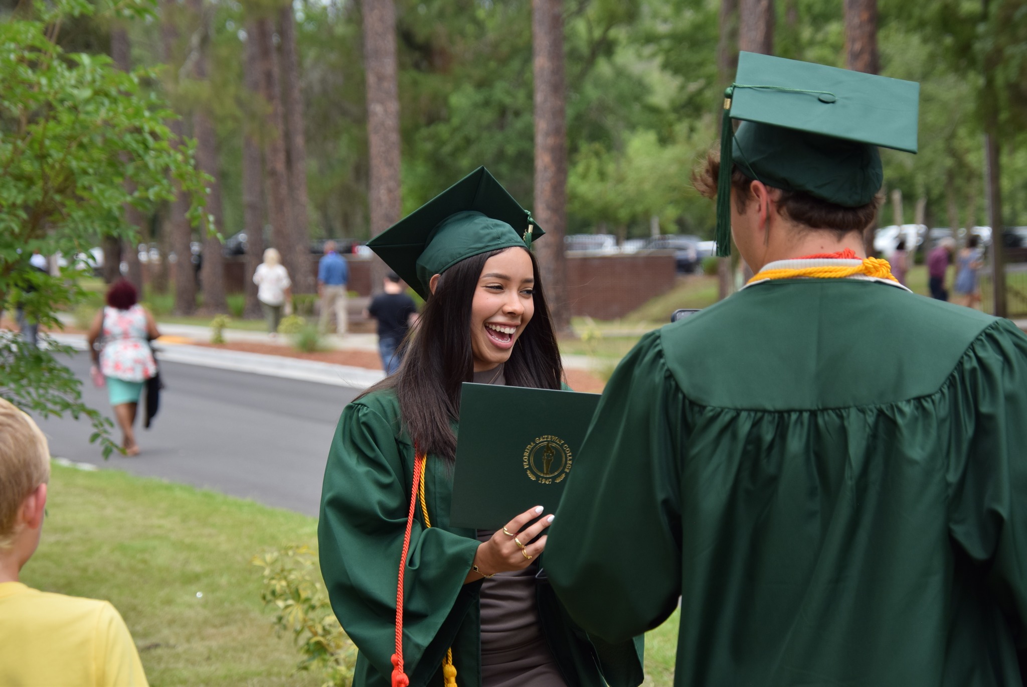 Smiling female graduate in green gown and cap, holding diploma.
