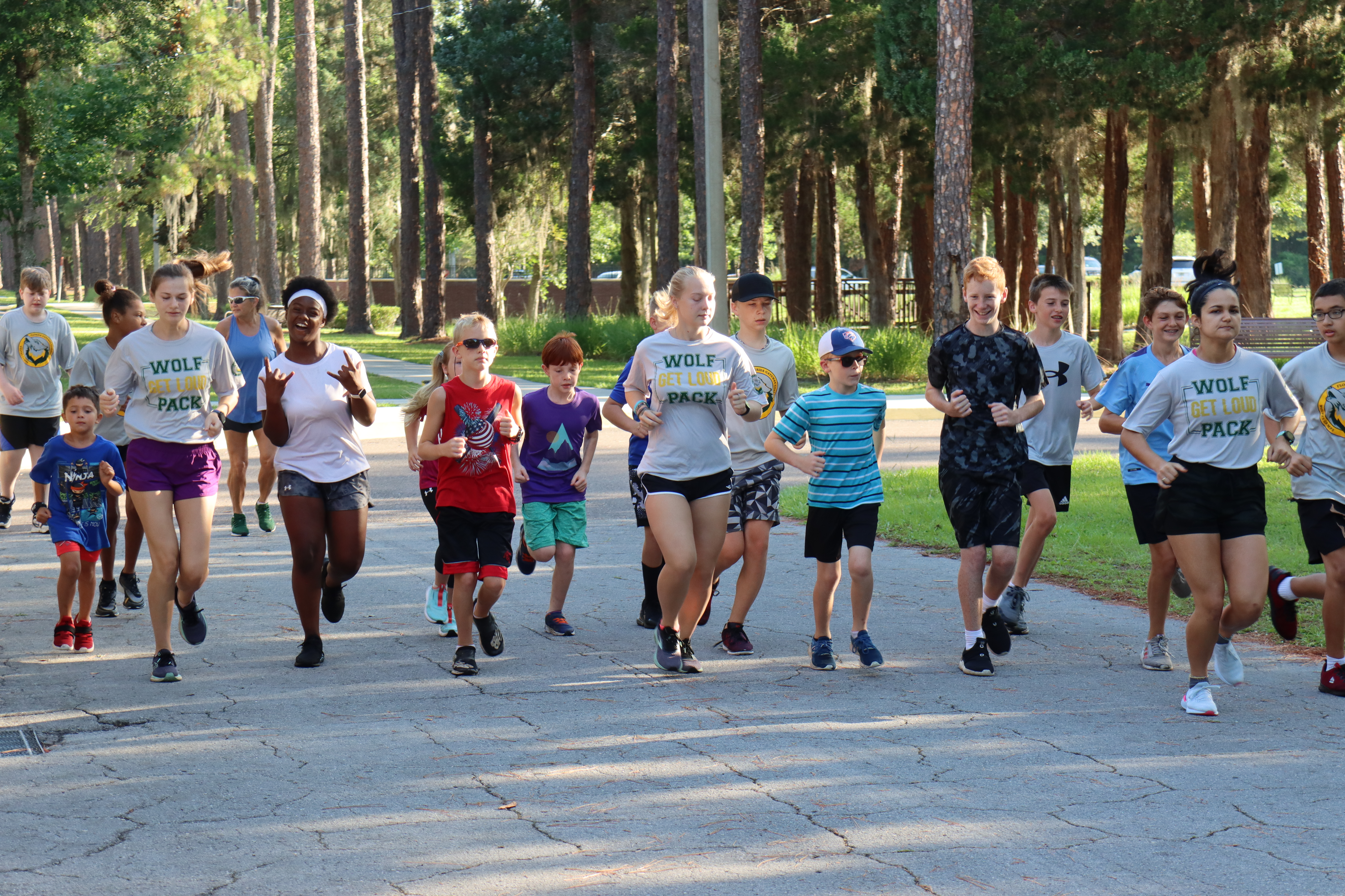 a group of young students running in a race, outdoors with trees in the background